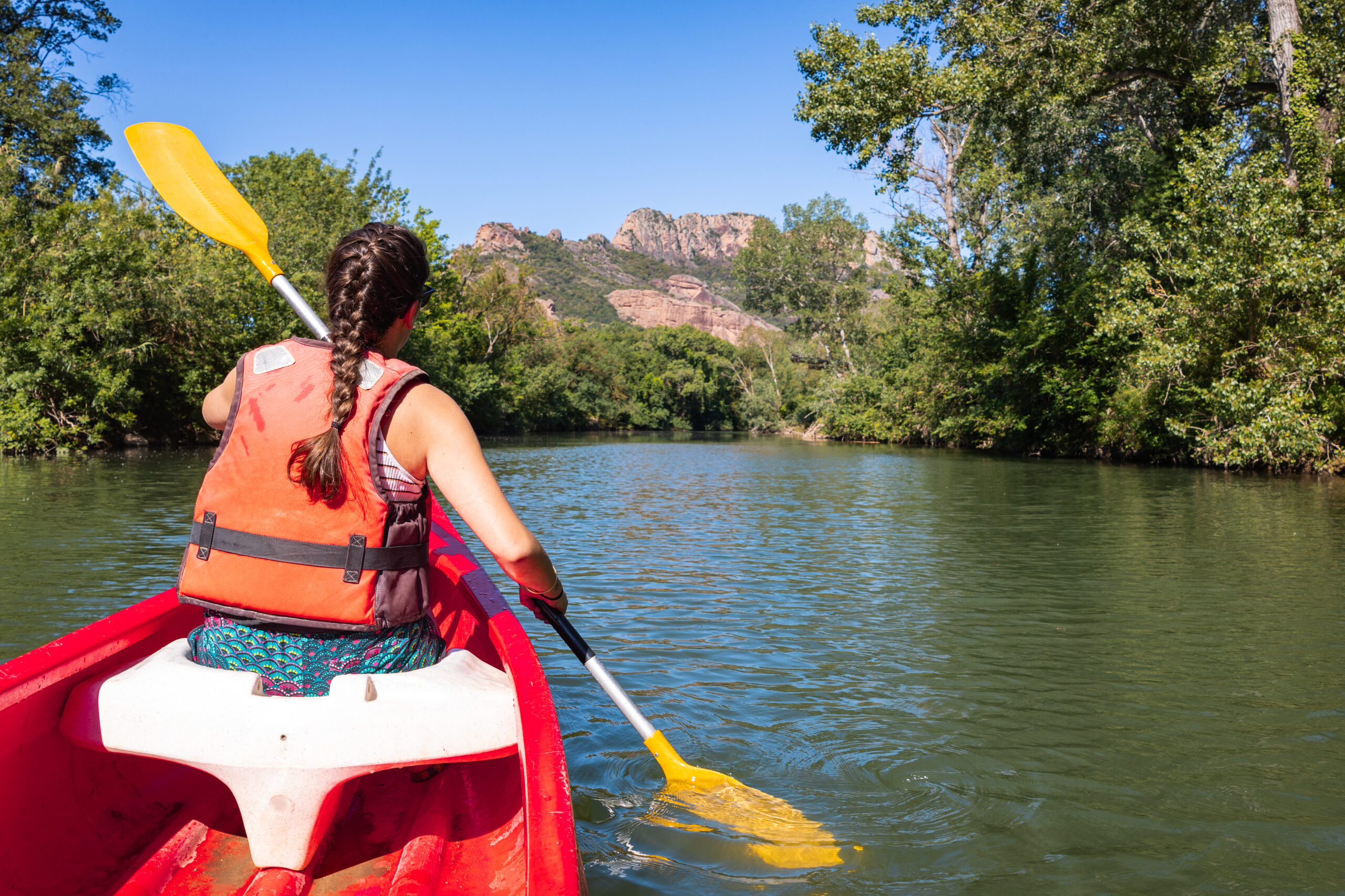 canoë sur l'argens avec une fille qui pagaie et un canoë rouge. on voit le rocher en fond