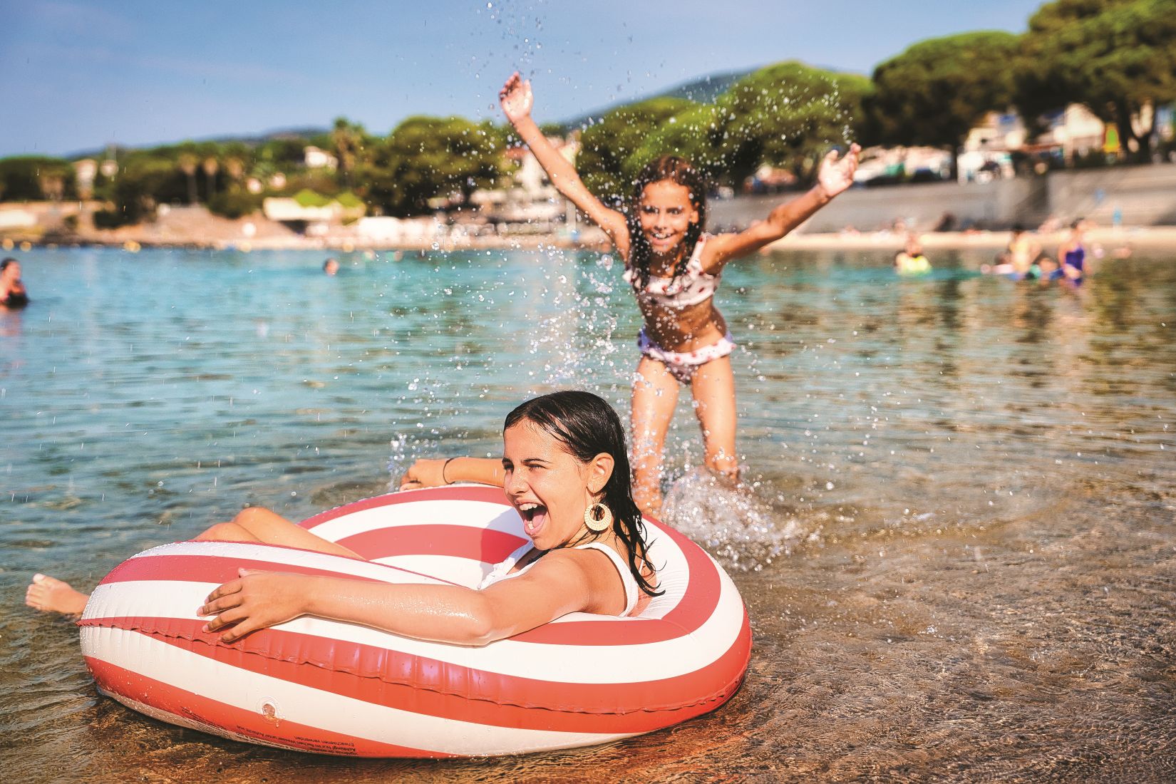deux enfants à la plage, une dans une bouée qui se fait éclaboussée par une autre