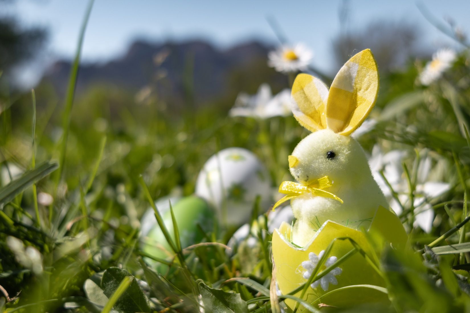 Lapin de Pâques décoratif dans un œuf jaune posé dans l’herbe avec fleurs printanières et rocher de Roquebrune en arrière-plan.