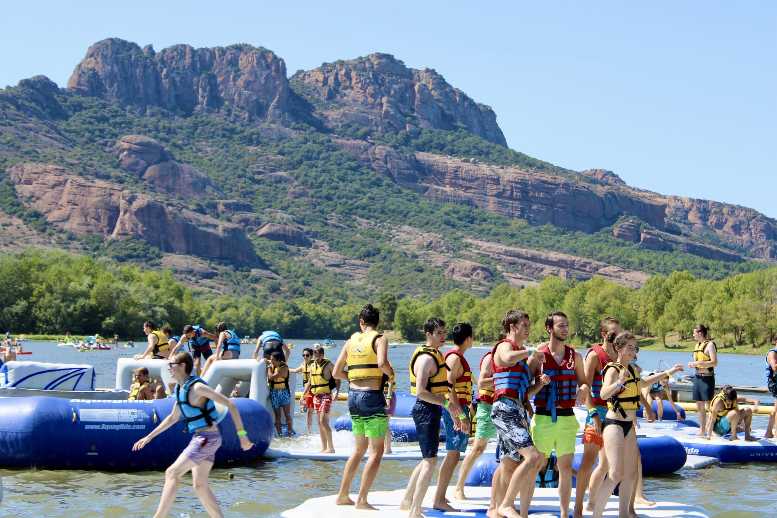 Participants profitant du parc aquatique gonflable du lac de l'Aréna à Roquebrune-sur-Argens avec le Rocher en arrière-plan.