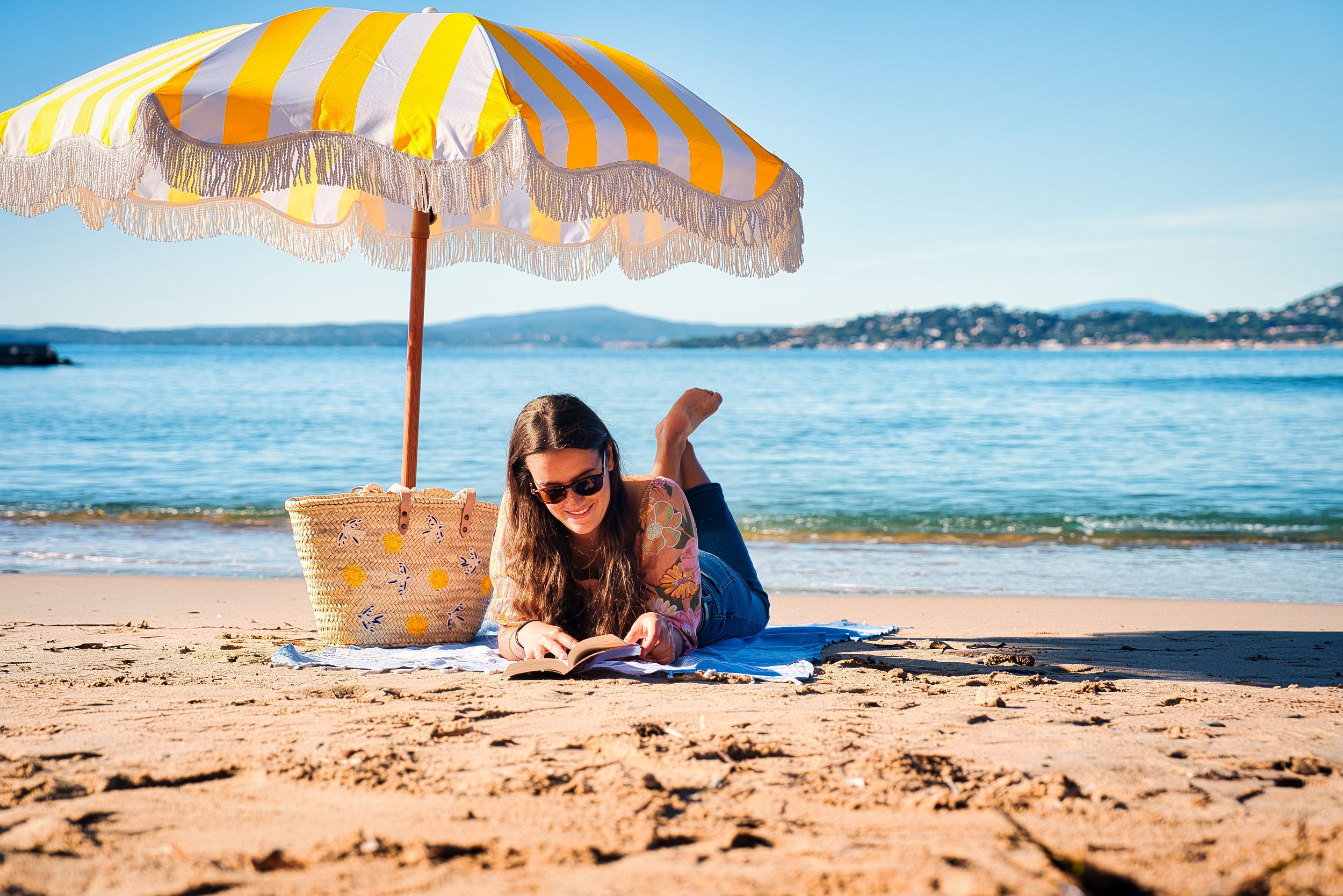 Femme lisant sur la plage des Issambres à Roquebrune-sur-Argens, sous un parasol face à la mer Méditerranée.