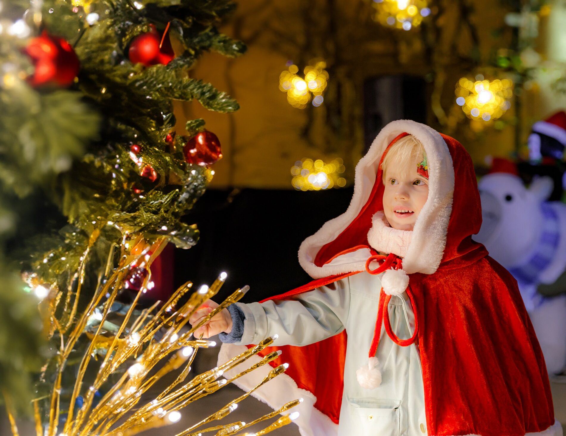Petite fille vêtue d'une cape de Noël admirant les décorations lumineuses et le sapin de Noël