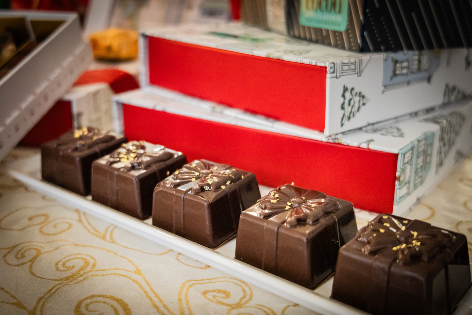 Chocolats artisanaux en forme de cadeaux de Noël, présentés devant des coffrets rouges et blancs à Roquebrune-sur-Argens.